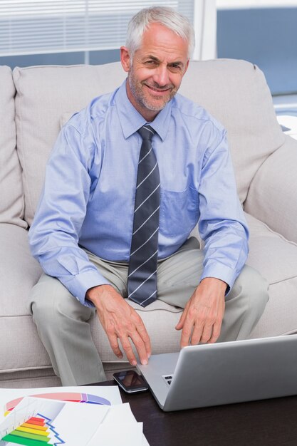 Geschäftsmann, der mit seinem Laptop arbeitet und an der Kamera lächelt