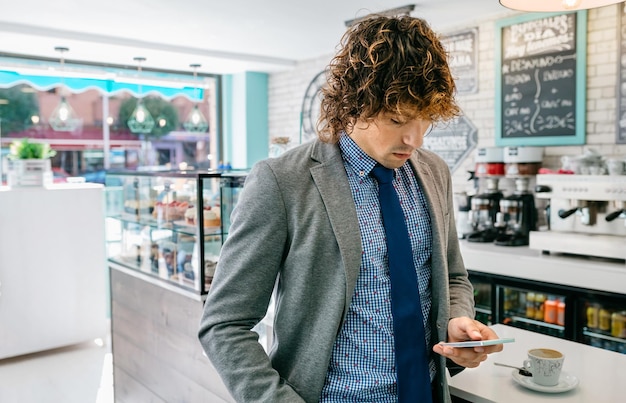 Geschäftsmann, der mobiles Stehen in einem Café betrachtet