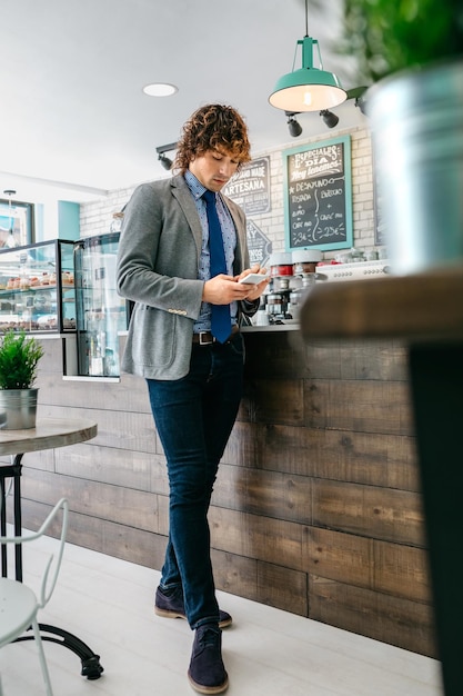 Geschäftsmann, der mobiles Stehen in einem Café betrachtet