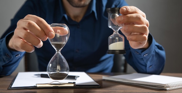 Geschäftsmann, der Sanduhr auf dem Tisch hält