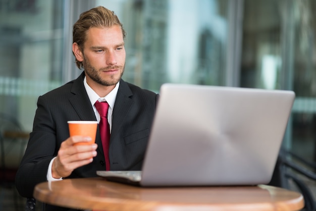 Geschäftsmann, der seinen Laptop beim Trinken des Kaffees verwendet