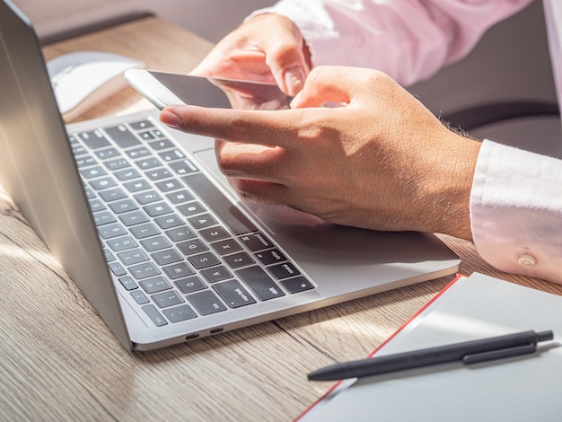 Geschäftsmann, der Smartphone benutzt, das am Morgen an seinem Schreibtisch im Büro an neuer Projektidee arbeitet