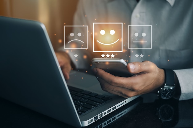 Geschäftsmann, der telefon mit virtuellem bildschirm auf dem glücklichen smiley-gesichtssymbol hält, um zufriedenheit im service zu geben. bewertung sehr beeindruckt. kundenservice und zufriedenheitskonzept