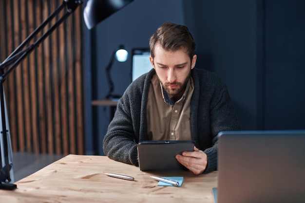 Geschäftsmann, der während der Nachtarbeit im Büro ein digitales Tablet verwendet