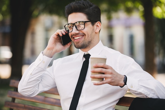 Geschäftsmann draußen im Park, der per Telefon Kaffee trinkt.