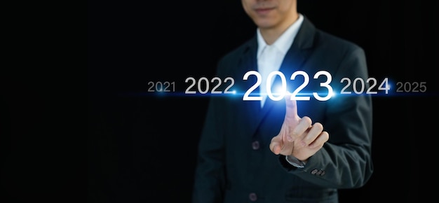 Foto geschäftsmann drückt und zeigt auf virtuellem bildschirm auf dunklem hintergrund mit kopie auf das jahr 2023