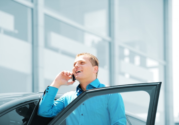 Geschäftsmann durch das Autoauto, sprechend am Handy und lächelt