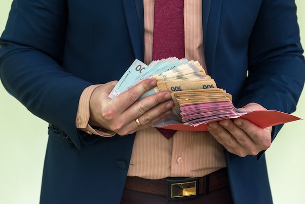 Geschäftsmann erhält Geld als Bestechungsgeld im Umschlag. ein Mann gibt einen ganzen Haufen ukrainisches Griwna-Geld in einem Umschlag