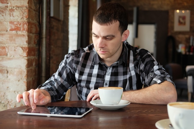 Geschäftsmann hält ein digitales Tablet und sitzt in einem Café.