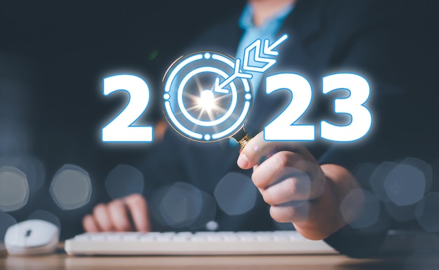 Geschäftsmann hält eine Vergrößerung mit Ziel-Symbol 2023 dunkler Hintergrund 2023 Konzept 2023 Neujahrsziel Ziel Aktionsplan Idee Inspiration Konzept