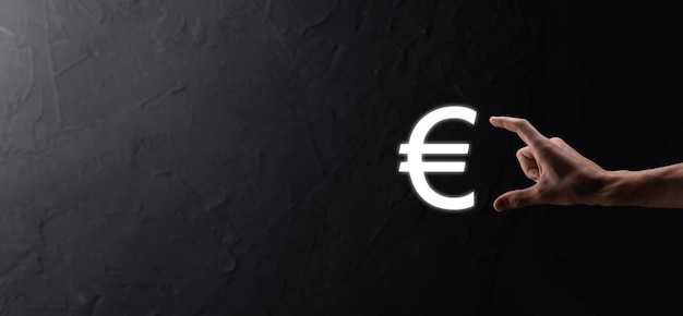 Geschäftsmann hält Geldmünzen-Symbole EUR oder Euro auf dunklem Hintergrund. Wachsendes Geldkonzept für Unternehmensinvestitionen und Finanzen