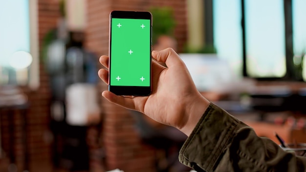 Geschäftsmann hält Greenscreen-Display auf dem Handy und analysiert leere Mockup-Vorlage mit isoliertem Copyspace. Modernes Smartphone mit Chroma-Key-Hintergrundbildschirm, das im Startbüro verwendet wird.