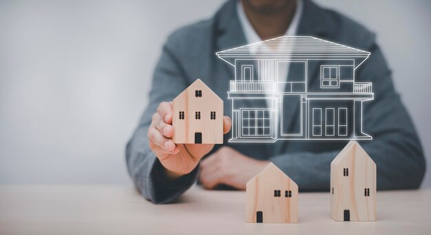 Geschäftsmann hält Mini-Holzhausmodell von einem Holztisch in der Hand, plant den Kauf von Immobilien, plant den Kauf der Immobilie. Konzept der Wählen Sie das Beste. Bau- und Architekturgeschäft.