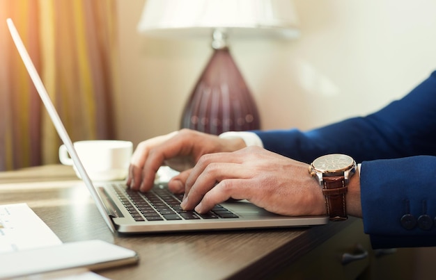 Geschäftsmann Hände tippen auf einem Laptop-Computer auf Holzschreibtisch im Hotelzimmer. Mann, der während der Bisiness-Reise arbeitet