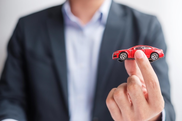 Geschäftsmann Hand hält rotes Auto Spielzeug Autoversicherung Garantievermietung Finanzielles Neu- und Reparaturkonzept