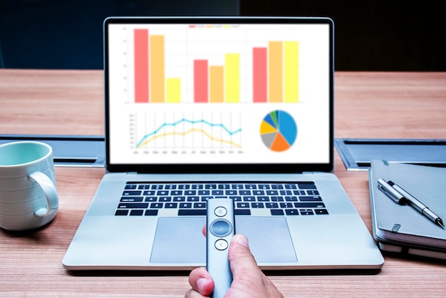 Geschäftsmann Hand halten Fernbedienungsfolie mit Mock-Up-Diagramm-Präsentation auf dem Display-Laptop