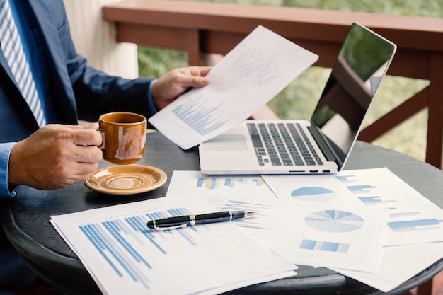 Geschäftsmann Hand mit Kaffeetasse, Analyse der Grafik mit Laptop im Home Office, um anspruchsvolle Geschäftsziele zu setzen und das neue Ziel zu erreichen