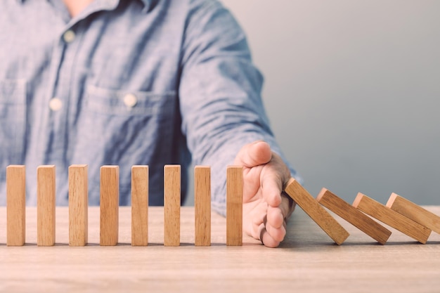 Geschäftsmann Hand stoppen Holzblock Domino auf dem Schreibtisch Ideen für Auswirkungen oder Risiken von Geschäftskrisen