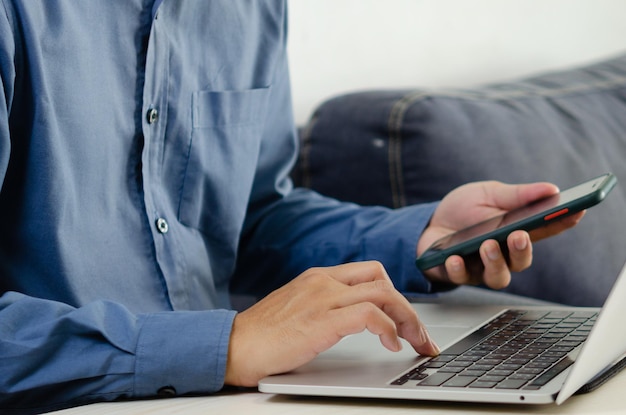 Geschäftsmann Hand tippen Tastatur auf Laptop-Computer mit Smartphone Close up Geschäftsmann Kommunikation Internet und Social Media an seinem Schreibtisch