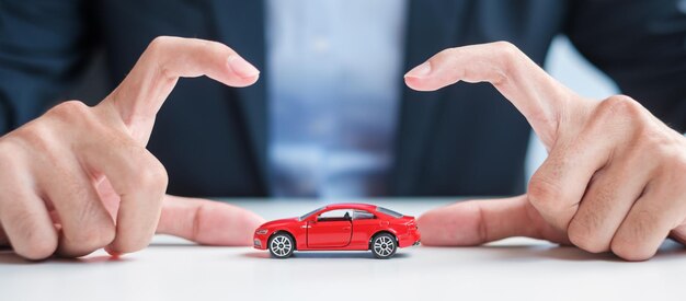 Geschäftsmann Handabdeckung oder Schutz rotes Auto Spielzeug auf dem Tisch Kfz-Versicherung Garantie Reparatur Financial Banking und Geldkonzept