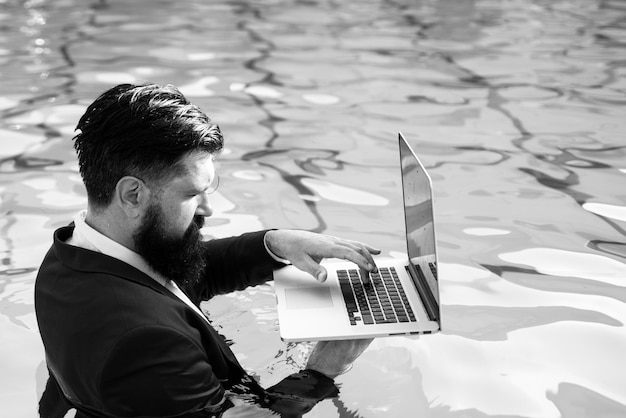 Geschäftsmann im Anzug mit Laptop am Swimmingpool