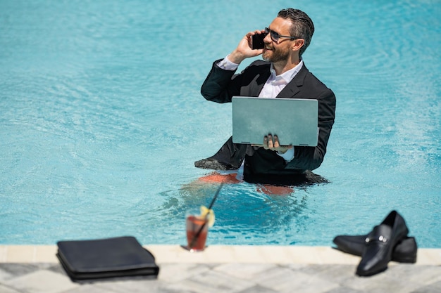 Geschäftsmann im Anzug mit Laptop im Schwimmbad Verrückter Geschäftsmann schwimmt im Sommerurlaub exci