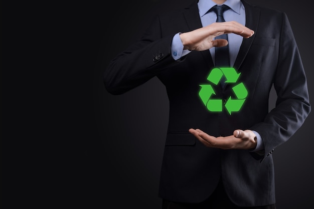 Geschäftsmann im Anzug über dunkler Oberfläche hält ein Recycling-Symbol, Zeichen in seinen Händen
