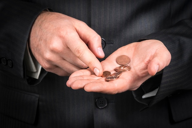 Geschäftsmann im Anzug zählt kleine Euro-Münzen in seiner Handfläche, Nahaufnahme
