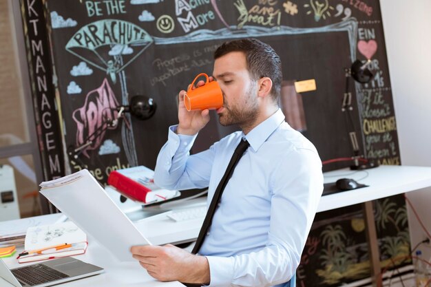 Geschäftsmann im Kreativbüro schaut sich Dokumente an und trinkt Kaffee