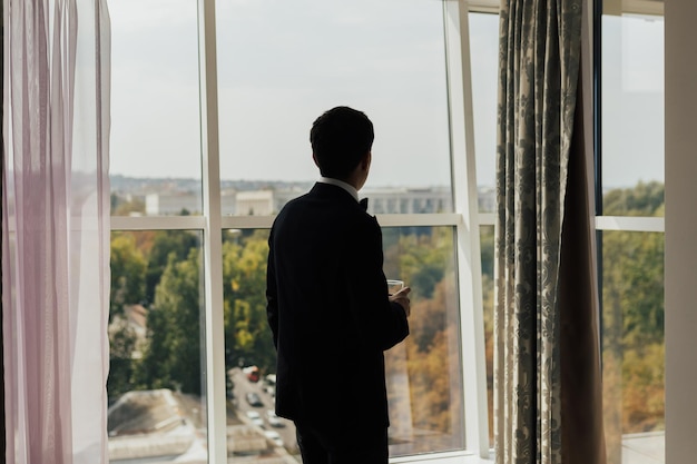 Geschäftsmann im schwarzen Anzug, der durch ein Panoramafenster auf eine Großstadt blickt