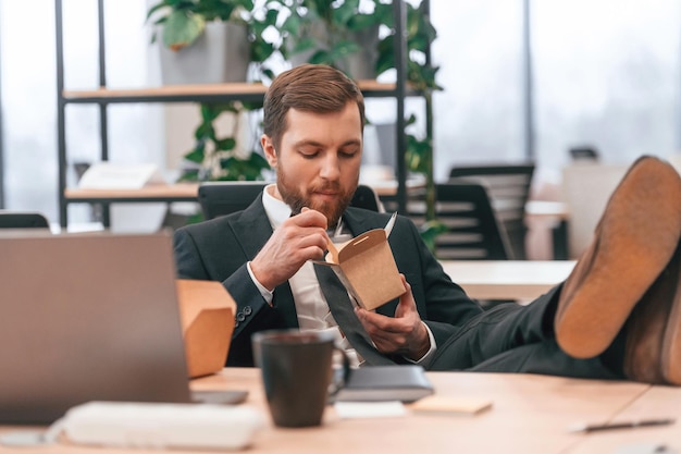 Foto geschäftsmann in anzug und krawatte sitzt im büro und isst lebensmittel aus der öko-box