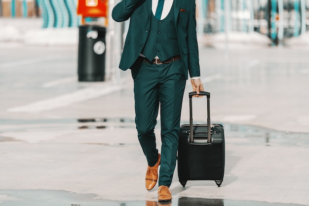 Geschäftsmann in der formellen Kleidung, die Gepäck zieht und auf der Straße geht. Geschäftsreisekonzept.
