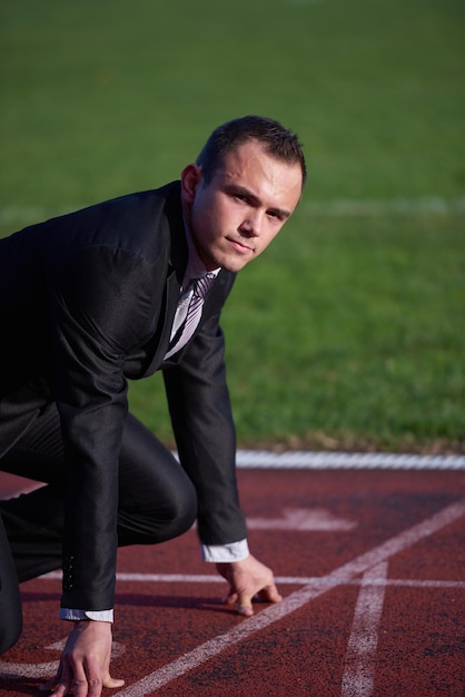 Geschäftsmann in Startposition, bereit zum Laufen und Sprinten auf der Leichtathletik-Rennstrecke