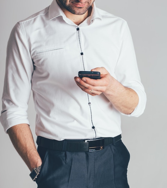 Geschäftsmann in weißem Hemd und schwarzer Hose steht und schreibt eine Nachricht vom Telefon in seine Hände im Büro. Nahansicht