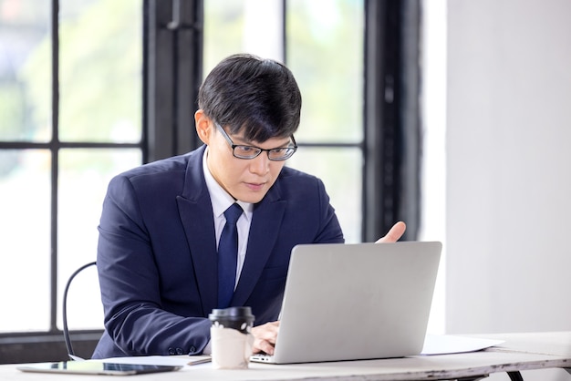 Geschäftsmann mit Brille, der an seinem Computer im Büro durch ein Fenster arbeitet