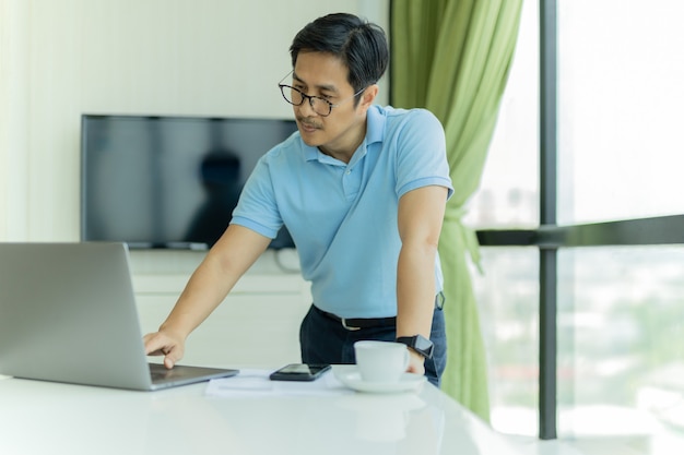 Geschäftsmann mit Brille, der sich über den Tisch beugt und am Laptop im Büro arbeitet work