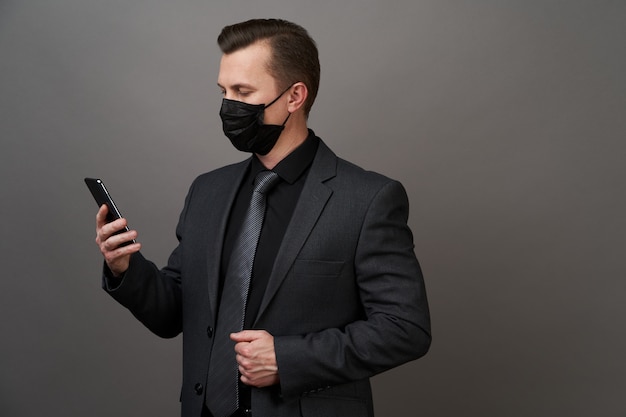 Geschäftsmann mit chirurgischer medizinischer Maske unter Verwendung des Mobiltelefons