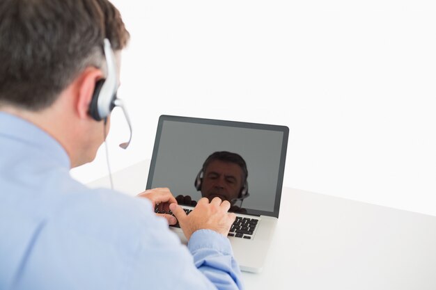 Geschäftsmann mit dem Kopfhörer, der an Laptop arbeitet