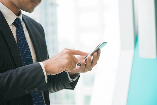 Geschäftsmann mit Handy-App Texting außerhalb des Büros in städtischen Stadt mit Wolkenkratzer Gebäude im Hintergrund. Junge kaukasischen Mann mit Smartphone für Business-Arbeit.