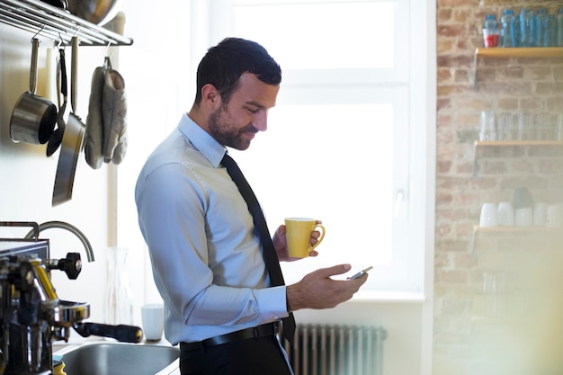 Geschäftsmann mit Kaffeepause in der Büroküche mit Blick auf das Handy