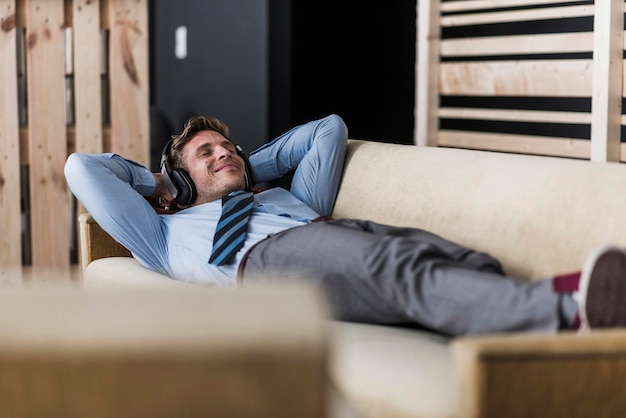 Geschäftsmann mit Kopfhörern liegt auf der Couch im Büro-Lounge