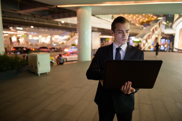 Geschäftsmann mit Laptop-Computer im Freien in der Nacht in der Stadt