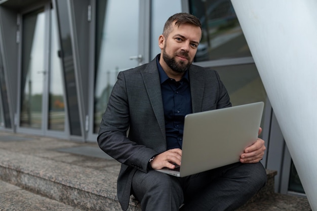Geschäftsmann mit Laptop sitzt auf den Stufen eines Bürogebäudekonzepts eines erfolgreichen Real