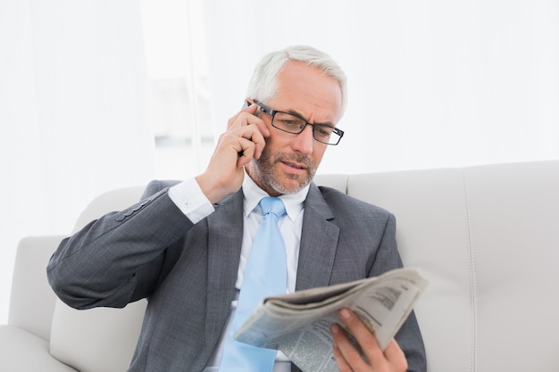 Geschäftsmann mit Mobiltelefon und Zeitung zu Hause