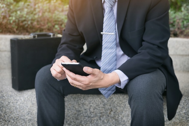 Geschäftsmann mit schwarzen Anzug und mit modernen Smartphone im Freien