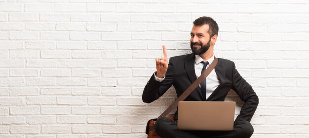 Geschäftsmann mit seinem Laptop, der auf dem Boden sitzt und einen Finger im Zeichen des Besten zeigt und anhebt