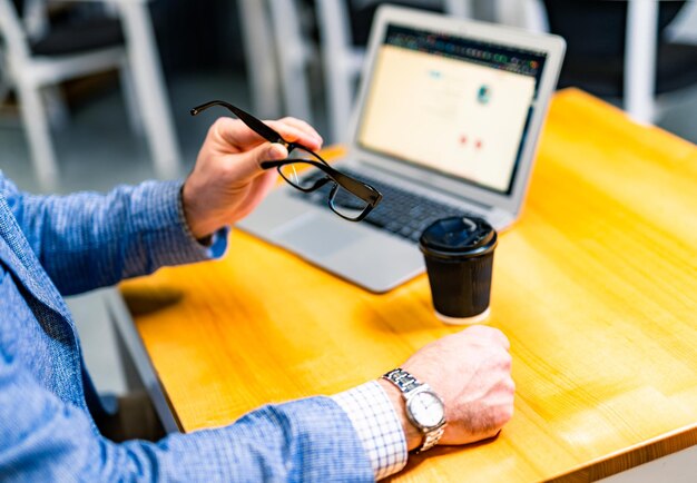 Geschäftsmann mit stylischer Brille in schwarzem Rand sitzt am Bürotisch Tasse Kaffee in der Nähe des Laptops