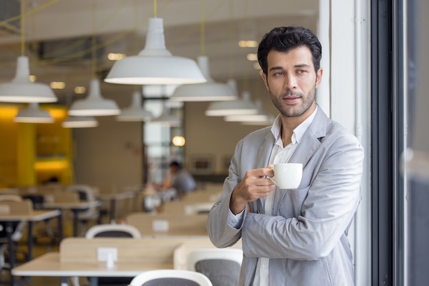 Geschäftsmann mit Tasse Kaffee, der aus dem Fenster im Büro schaut