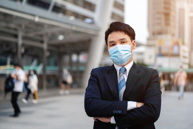 Geschäftsmann mit verschränkten Armen und tragender medizinischer Maske während der Coronavirus-Pandemie in der Stadt