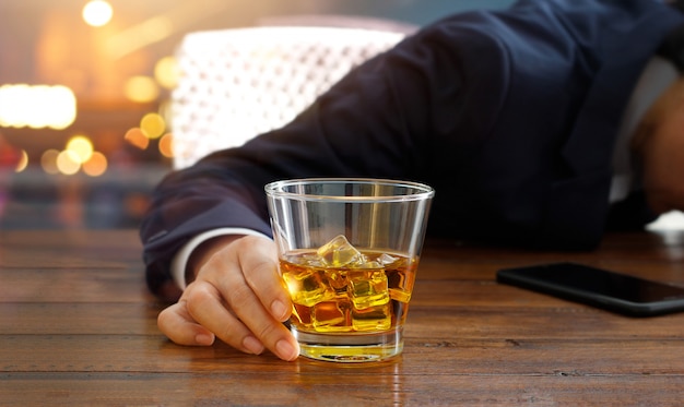 Geschäftsmann mit Whisky Bourbon in der Hand, betrunken am Tisch in der Kneipe schlafen